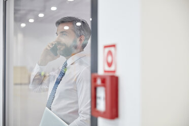 Männlicher Vorgesetzter, der am Fenster in einer Fabrik mit seinem Handy telefoniert - CAIF07167