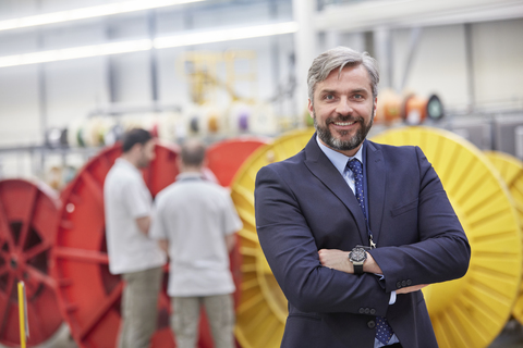 Porträt eines lächelnden, zuversichtlichen Geschäftsmannes in einer Fabrik für Glasfasertechnik, lizenzfreies Stockfoto