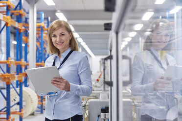 Portrait smiling female supervisor with clipboard in fiber optics factory - CAIF07186