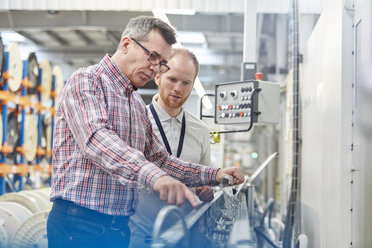 Männlicher Vorgesetzter und Arbeiter bei der Überprüfung von Maschinen in einer Glasfaserfabrik - CAIF07190