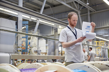 Männlicher Vorgesetzter mit Klemmbrett bei der Überprüfung des Inventars in einer Fabrik für Glasfasertechnik - CAIF07196