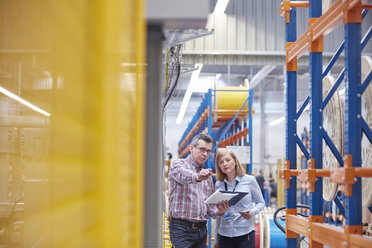 Männliche und weibliche Manager mit Klemmbrett im Gespräch in einer Fabrik für Glasfasertechnik - CAIF07200