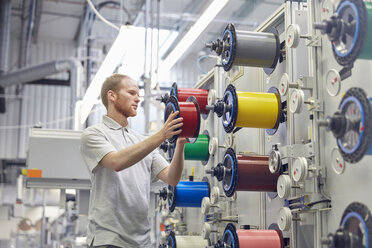 Männlicher Arbeiter wechselt Spulen an Maschinen in einer Glasfaserfabrik - CAIF07201