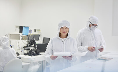 Porträt einer lächelnden Ingenieurin im Schutzanzug mit Papierkram in einem Forschungs- und Prüflabor für Glasfasertechnik - CAIF07204