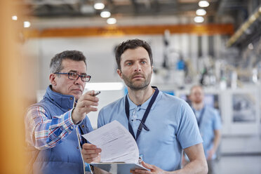 Serious male supervisors with clipboard talking in factory - CAIF07222