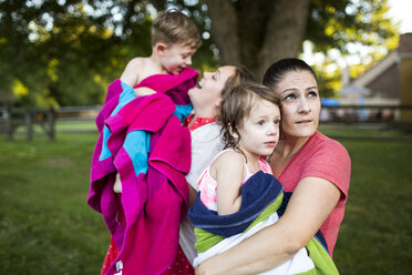 Lesbische Mütter halten nasse Kinder in einem Handtuch eingewickelt im Sommer Hof - CAIF07232