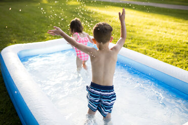 Geschwister im Vorschulalter spielen und planschen im aufblasbaren Schwimmbecken - CAIF07234