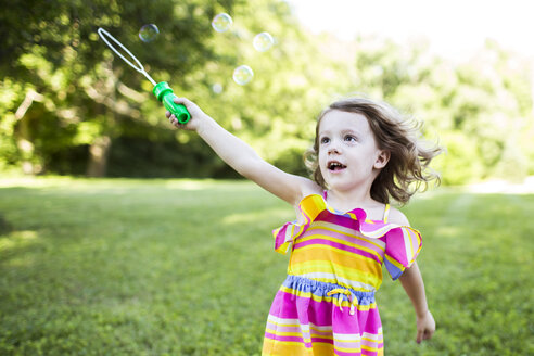 Preschool girl playing with bubble wand in summer yard - CAIF07235