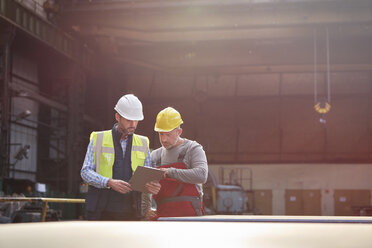 Männlicher Vorarbeiter und Arbeiter mit Klemmbrett im Gespräch in einer Fabrik - CAIF07241