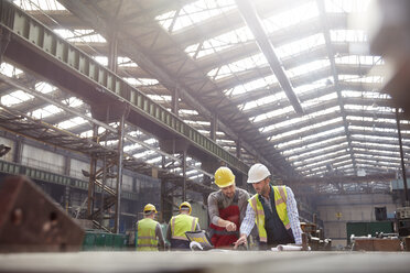 Male foreman and engineer with laptop meeting in factory, discussing blueprints - CAIF07244