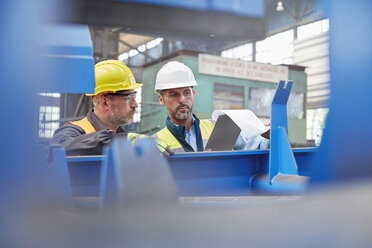Männlicher Vorarbeiter und Arbeiter bei der Durchsicht von Papierkram in einer Fabrik - CAIF07252