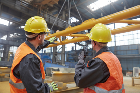 Männliche Arbeiter beobachten das Anheben der Ausrüstung in der Fabrik, lizenzfreies Stockfoto