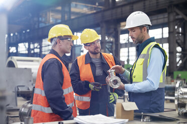 Männliche Ingenieure diskutieren in der Fabrik über ein Stahlteil - CAIF07259