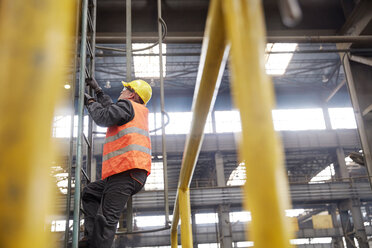 Männlicher Arbeiter klettert in einer Fabrik auf eine Leiter - CAIF07262