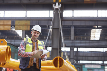 Portrait confident male foreman writing on clipboard in factory - CAIF07263