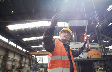 Männlicher Arbeiter, der eine Maschine an einem Schaltpult bedient, gestikuliert - CAIF07264