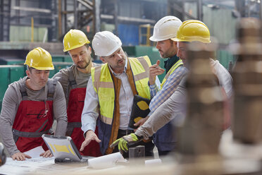 Männlicher Vorarbeiter, Ingenieure und Arbeiter bei einer Laptop-Besprechung, bei der Blaupausen in einer Fabrik diskutiert werden - CAIF07266