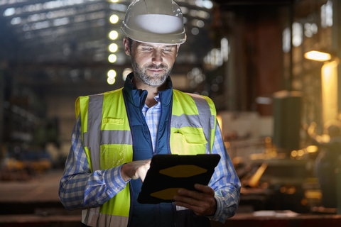 Männlicher Ingenieur arbeitet an einer leuchtenden digitalen Tafel in einer dunklen Fabrik, lizenzfreies Stockfoto