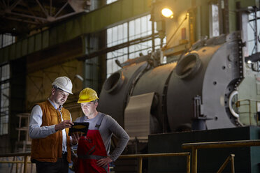 Ein männlicher Ingenieur und ein Arbeiter benutzen ein digitales Tablet in einer dunklen Fabrik - CAIF07270