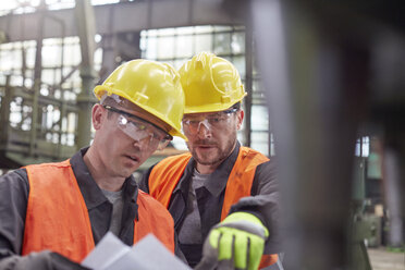 Männliche Arbeiter besprechen Papierkram in einer Fabrik - CAIF07272