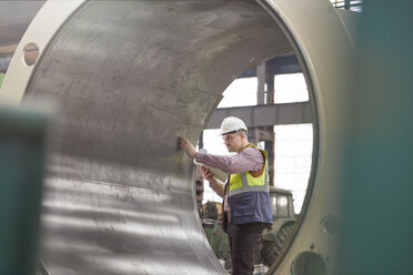 Männlicher Ingenieur, der einen großen Stahlzylinder in einer Fabrik untersucht - CAIF07276