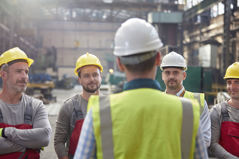 Männlicher Vorarbeiter im Gespräch, Treffen mit Arbeitern in einer Fabrik, lizenzfreies Stockfoto