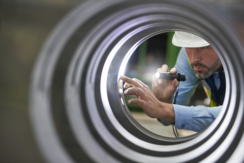 Männlicher Ingenieur mit Taschenlampe bei der Inspektion eines Stahlzylinders, lizenzfreies Stockfoto