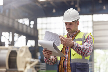 Male foreman reviewing paperwork on clipboard in factory - CAIF07279