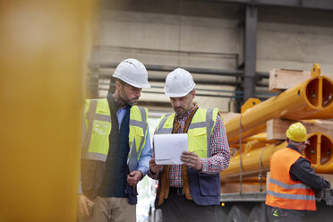 Männlicher Vorarbeiter und Arbeiter bei der Durchsicht von Papierkram in einer Fabrik - CAIF07281