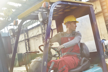 Male worker driving forklift, backing up in factory - CAIF07288