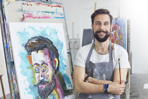 Porträt eines lächelnden, selbstbewussten männlichen Künstlers, der in einem Kunstatelier malt - CAIF07307