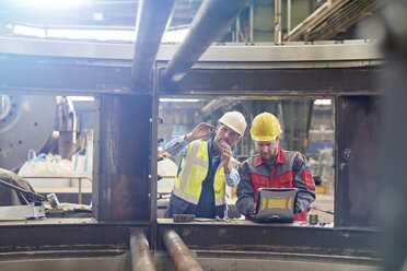 Männliche Ingenieure mit Laptop bei der Prüfung von Teilen in einer Fabrik - CAIF07324