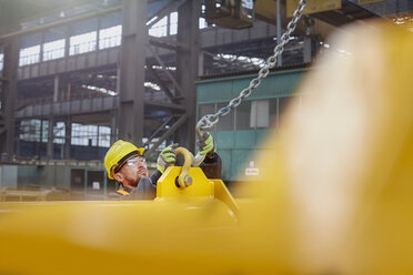 Male factory worker attaching chain to equipment - CAIF07325