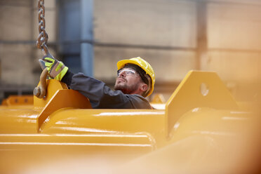 Männlicher Arbeiter, der eine Kette an einer Anlage in einer Fabrik befestigt - CAIF07327