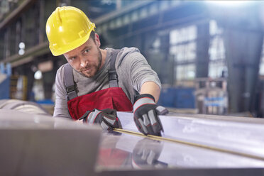 Fokussierter männlicher Arbeiter, der Stahl in einer Fabrik untersucht - CAIF07336