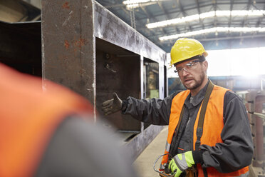 Männlicher Arbeiter, der einem Kollegen in einer Fabrik ein Stahlteil erklärt - CAIF07341