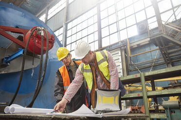 Männlicher Vorarbeiter und Ingenieur bei der Durchsicht von Blaupausen in einer Fabrik - CAIF07342