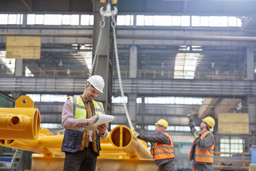 Male foreman with clipboard standing near workers in factory - CAIF07343