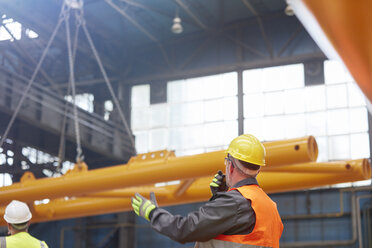 Männlicher Arbeiter mit Walkie-Talkie, der das Absenken von Maschinen in einer Fabrik anleitet - CAIF07347