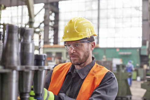 Fokussierter männlicher Arbeiter, der Stahlteile in einer Fabrik untersucht - CAIF07351