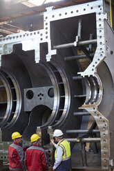 Male workers examining large steel equipment in factory - CAIF07353