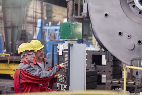Männliche Arbeiter bedienen Maschinen an einem Schaltpult in einer Fabrik - CAIF07356