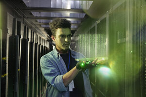 Male IT technician holding glowing futuristic digital tablet in server room - CAIF07364
