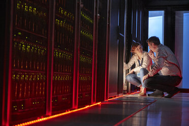 IT technicians talking at glowing panel in dark server room - CAIF07372