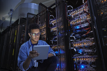 Fokussierter männlicher IT-Techniker mit digitalem Tablet in einem dunklen Serverraum - CAIF07378