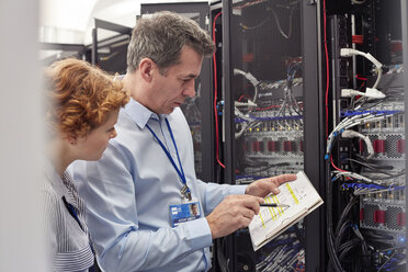 IT technicians with clipboard examining panel in server room - CAIF07380