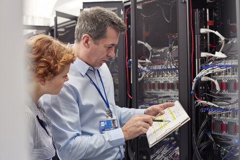 IT-Techniker mit Klemmbrett bei der Untersuchung der Tafel im Serverraum - CAIF07380