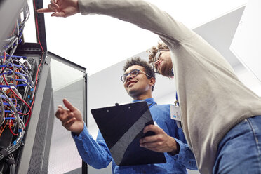 Male IT technicians with clipboard talking at panel in server room - CAIF07382