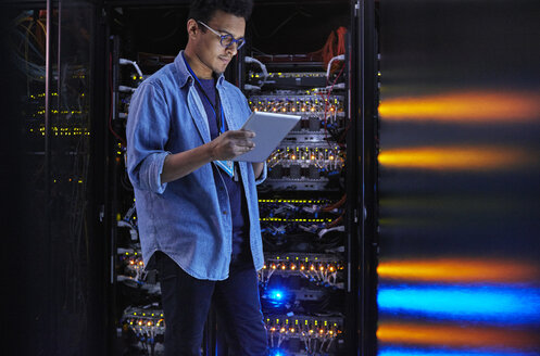 Fokussierter männlicher IT-Techniker, der ein digitales Tablet an einer Tafel in einem dunklen Serverraum benutzt - CAIF07383