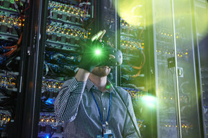 Male computer programmer using virtual reality simulator glasses and glowing glove in server room - CAIF07384